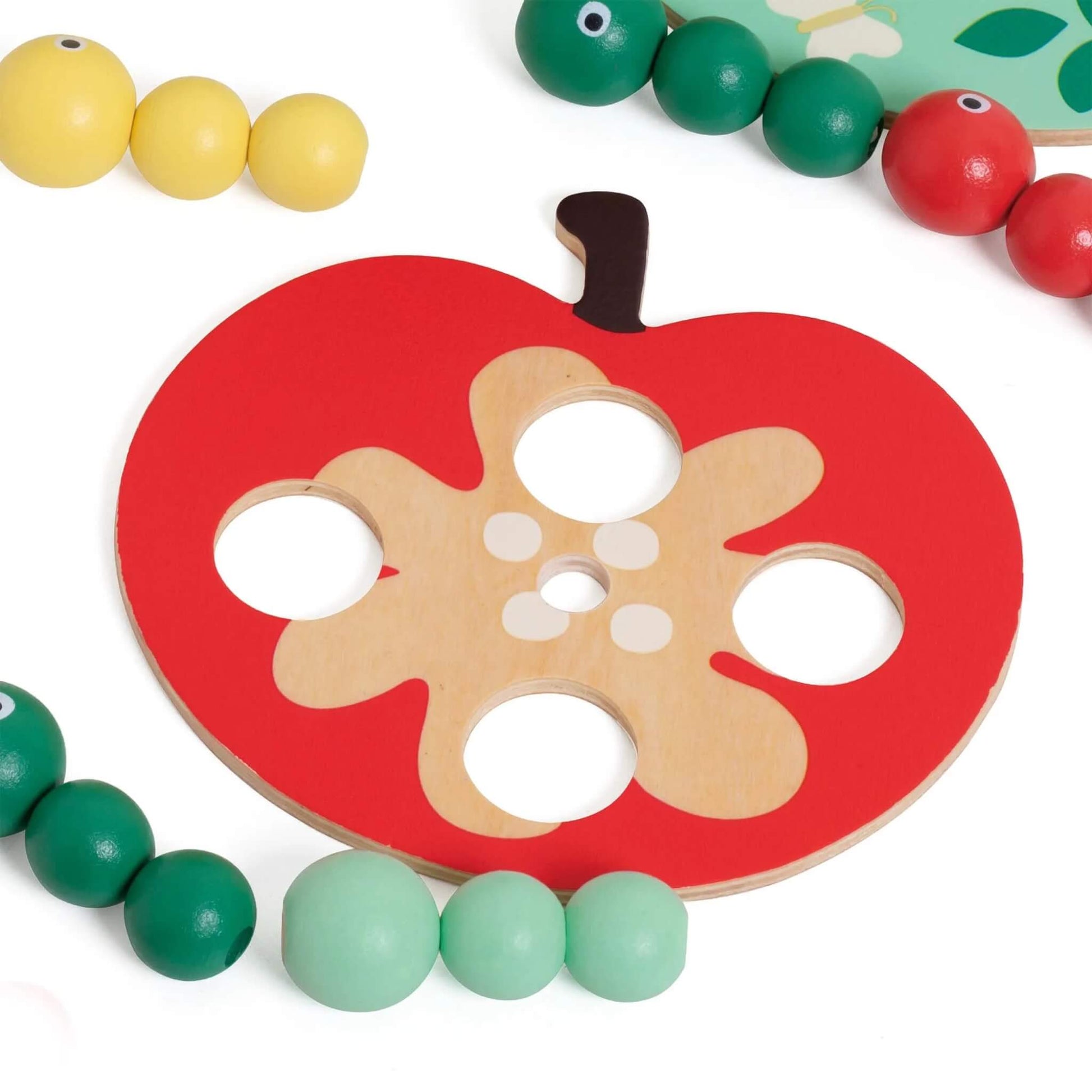 Flat red toy apple piece with holes, placed beside green, red, and yellow toy caterpillars made of small wooden beads.