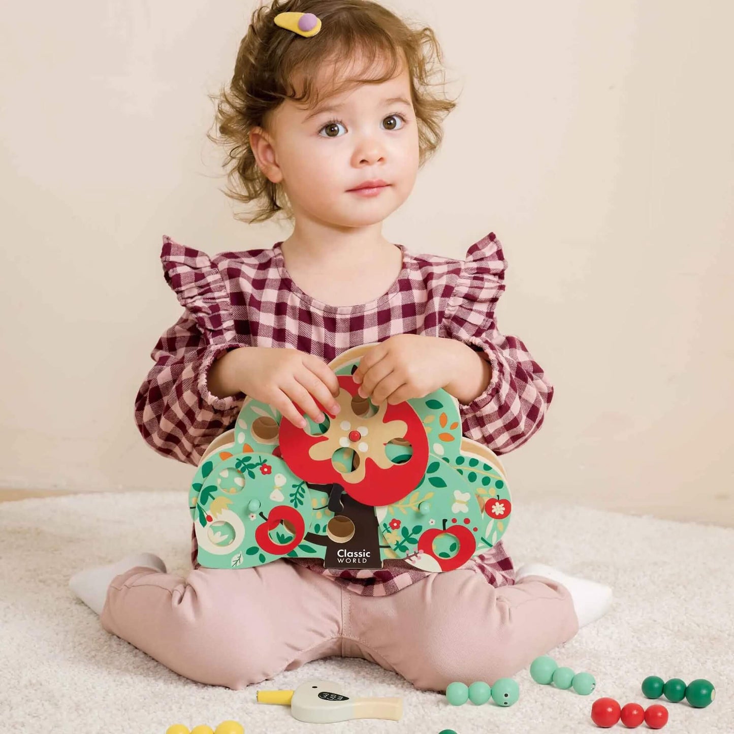Young child sitting on a carpet, holding the Classic World Doctor Woodpecker toy with magnetic bird and wooden caterpillar pieces spread around.