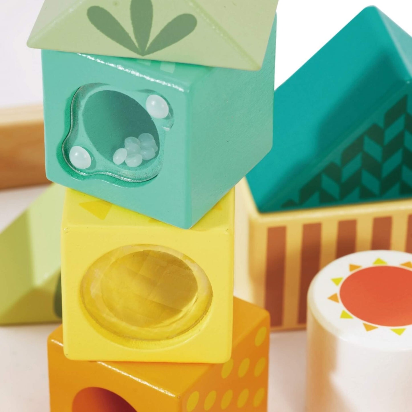 A close-up of stacked wooden blocks showing translucent panels with small beads inside, painted in teal and yellow with smooth rounded edges.