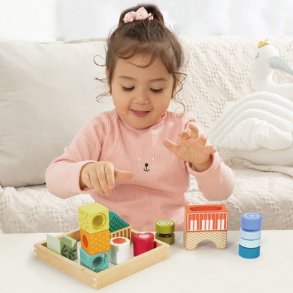 A child seated at a table playing with wooden sensory blocks, arranging shapes and exploring beads, colours, and cut-out features.