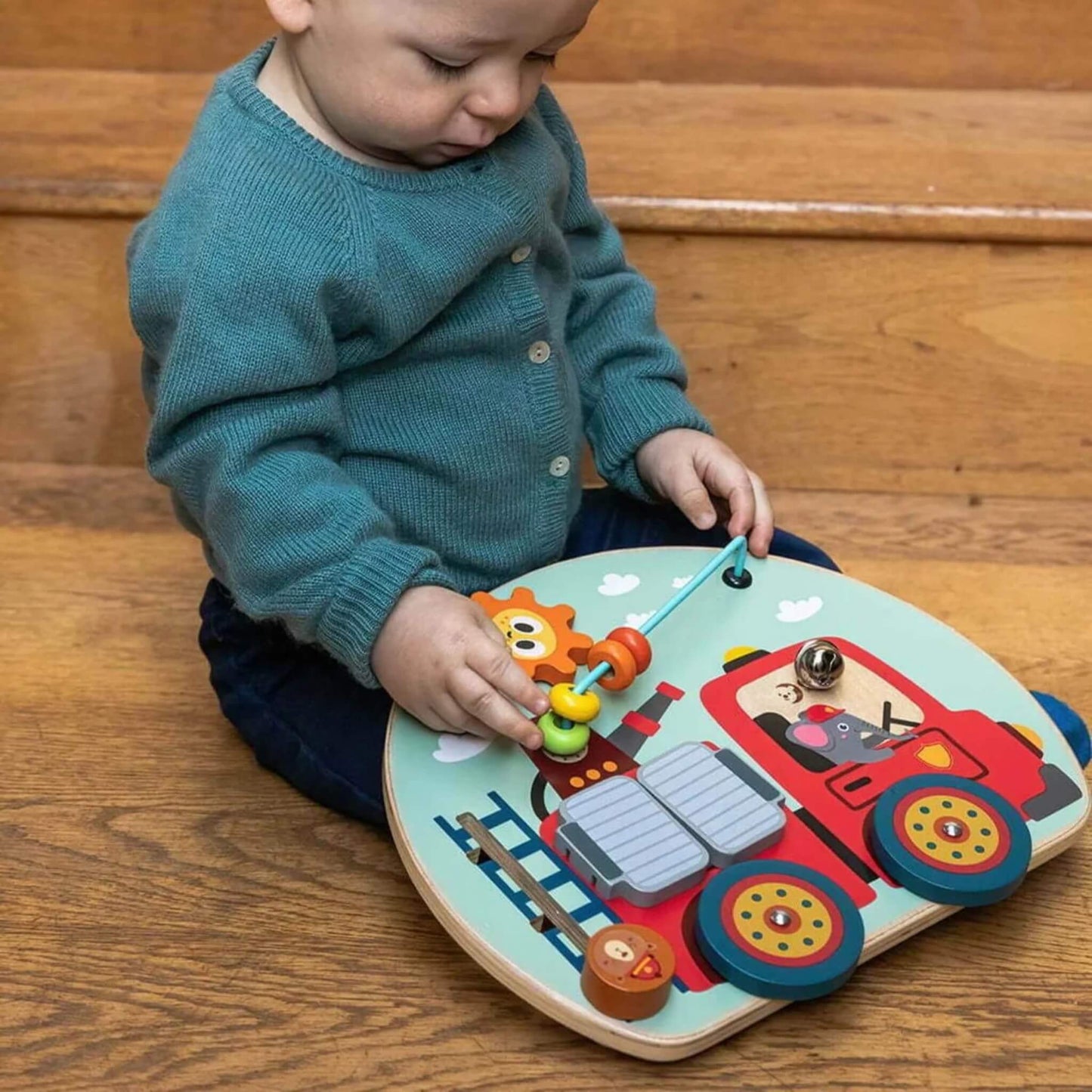 Baby sitting by stairs, sliding the busy board’s colourful beads along the blue wire.