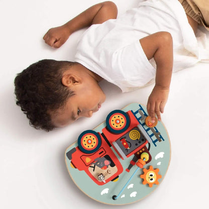 Young child lying on the floor, playing with the busy board and moving the fireman figure. up the ladder.