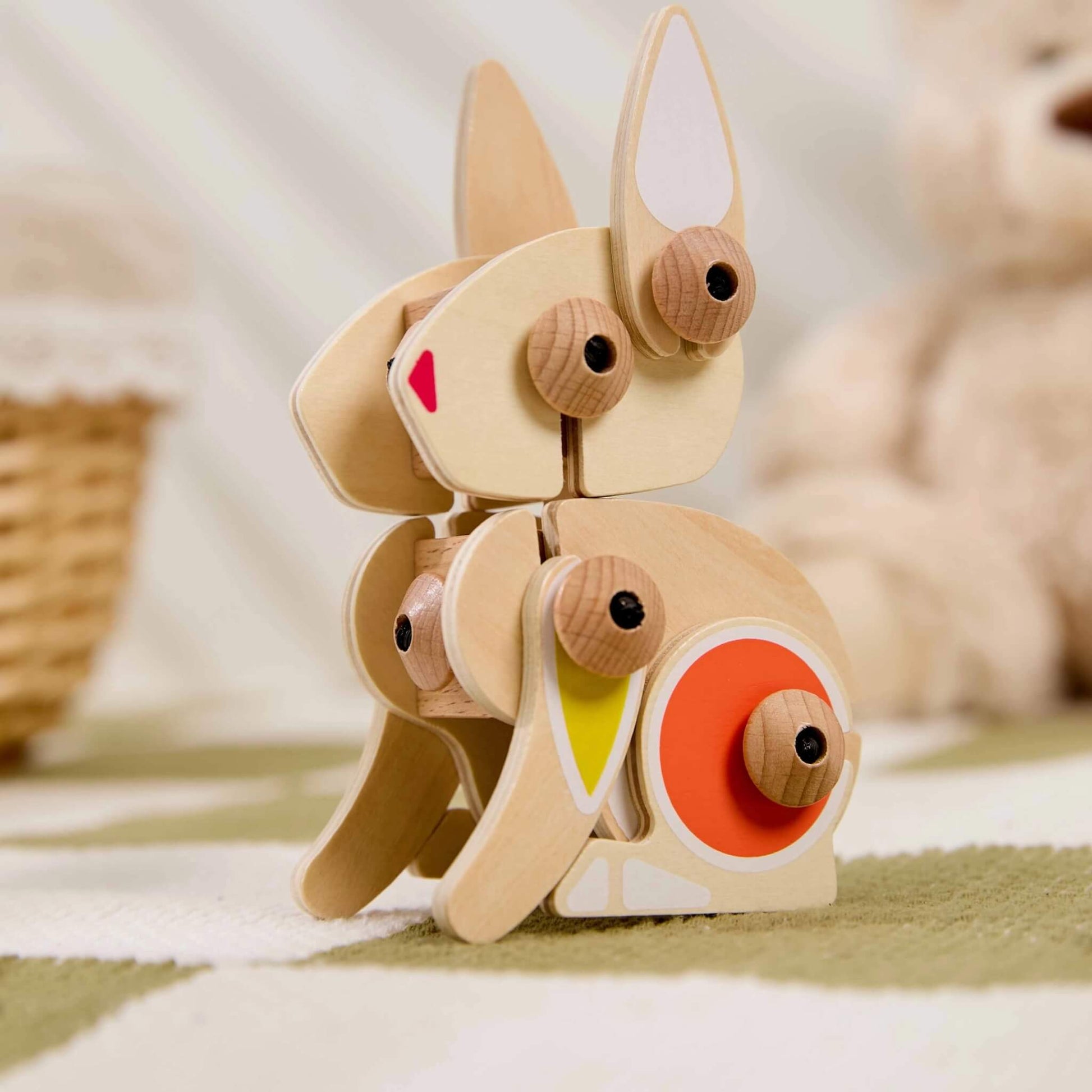 Wooden rabbit construction toy with long ears and jointed legs posed sitting on a soft textured play mat with natural wood finish.