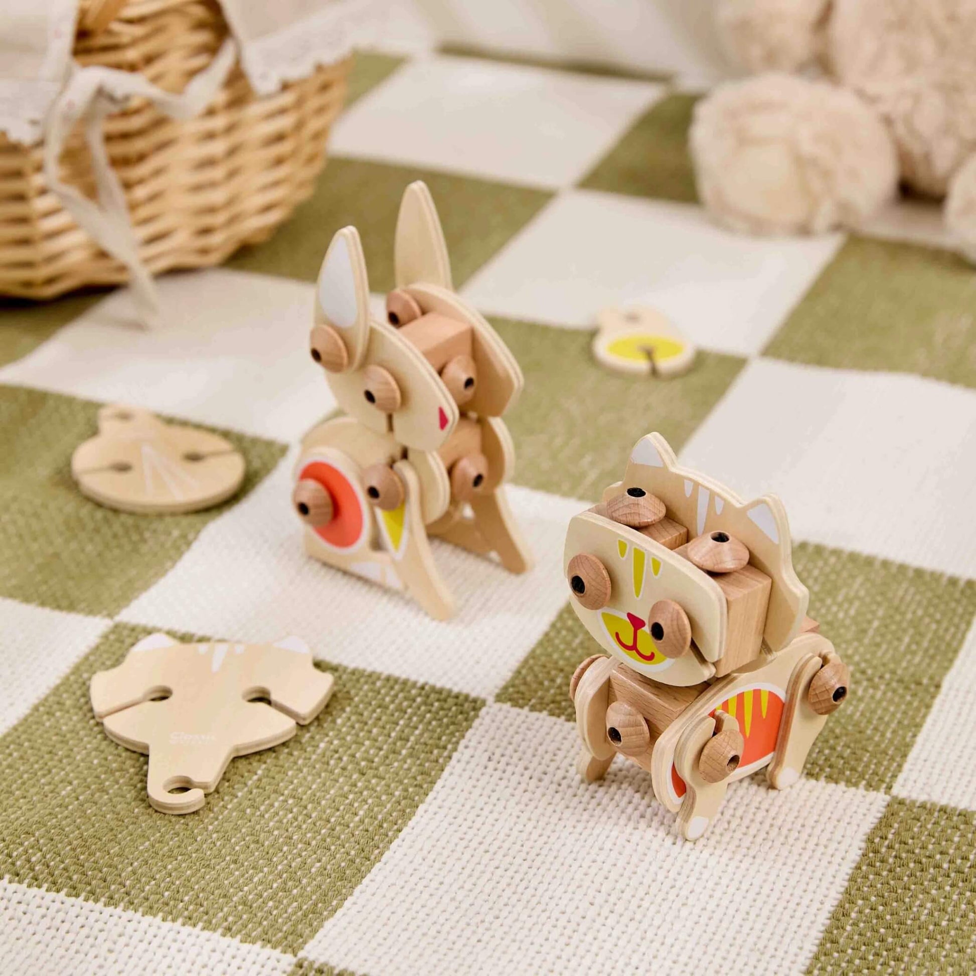 Two wooden animal construction toys assembled as a rabbit and cat placed on a play mat with loose pieces nearby showing buildable design.
