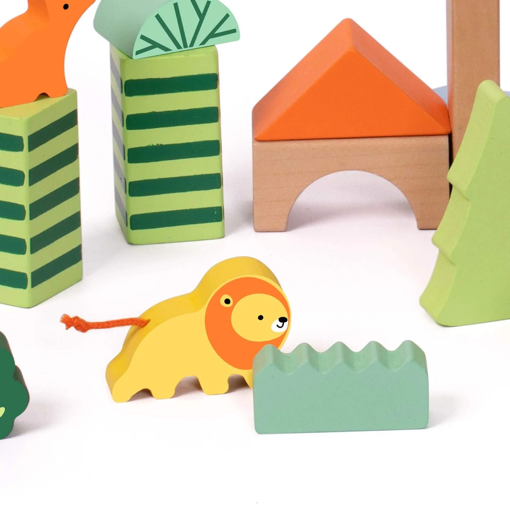 Close-up of a yellow wooden lion with an orange mane and string tail, standing near green-striped and orange geometric blocks shaped like trees and houses.