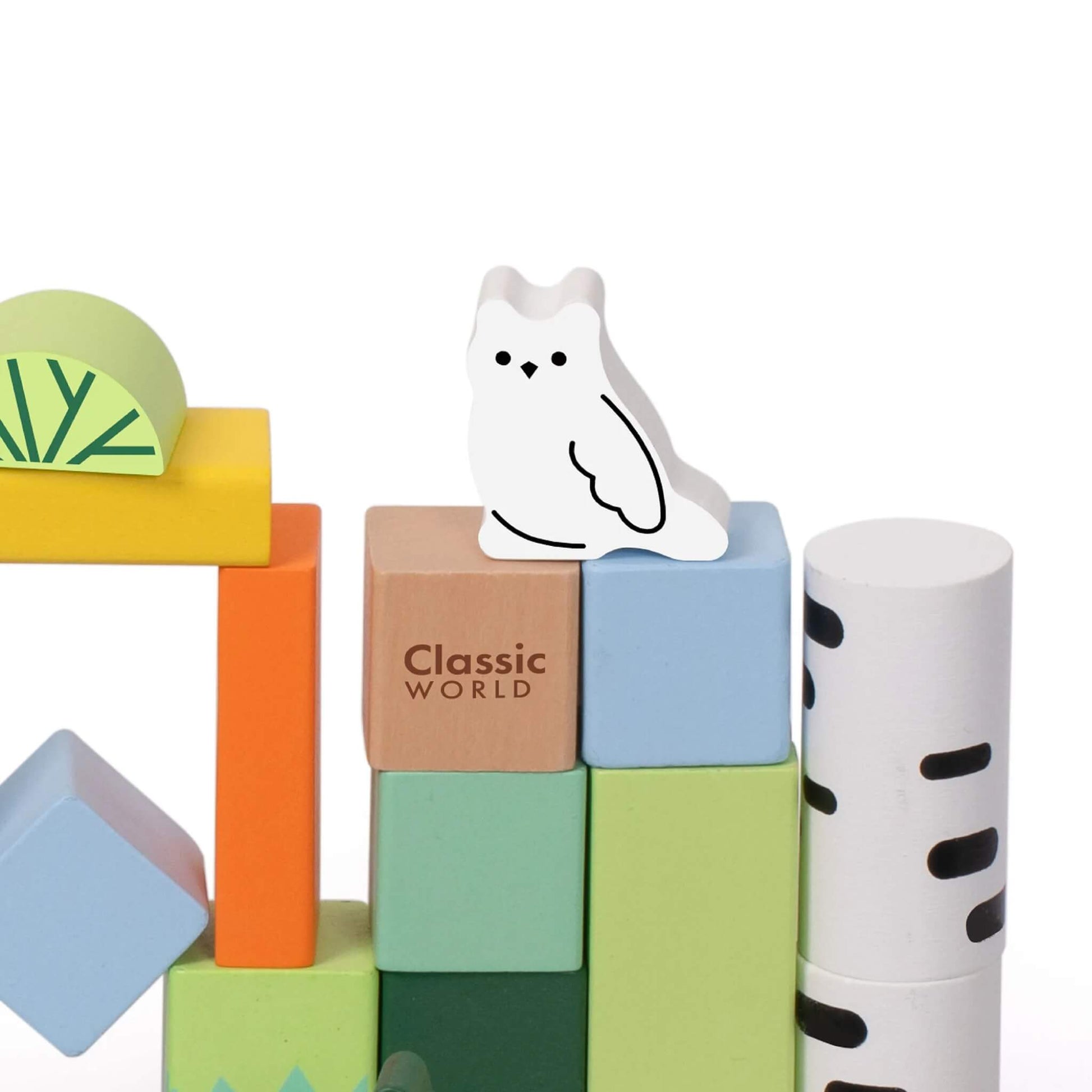 Close-up of a white owl wooden figure perched on top of stacked wooden blocks, with a birch-patterned cylinder and Classic World logo block nearby.