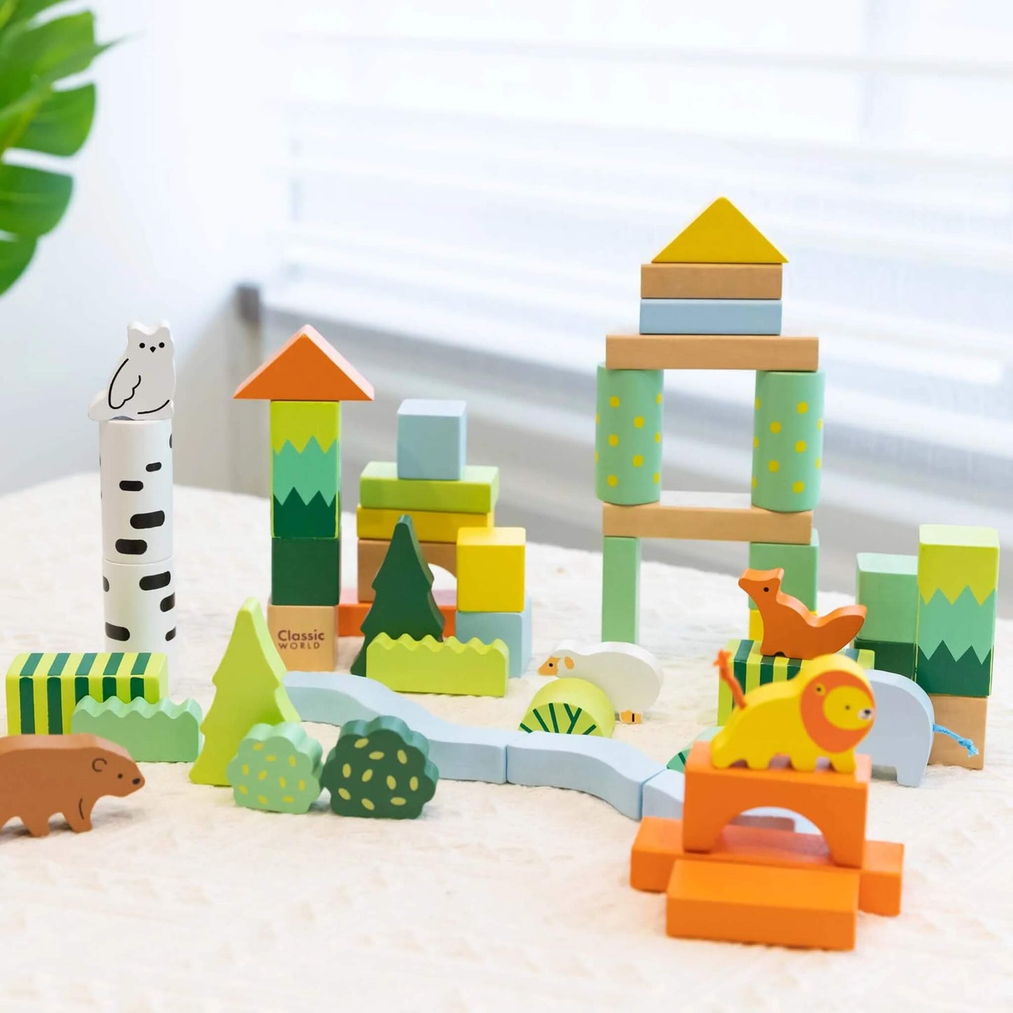Forest block set displayed on a table near a window, showing a playful scene of stacked towers, trees, and animals like a lion, fox, owl, elephant, sheep, and bear.