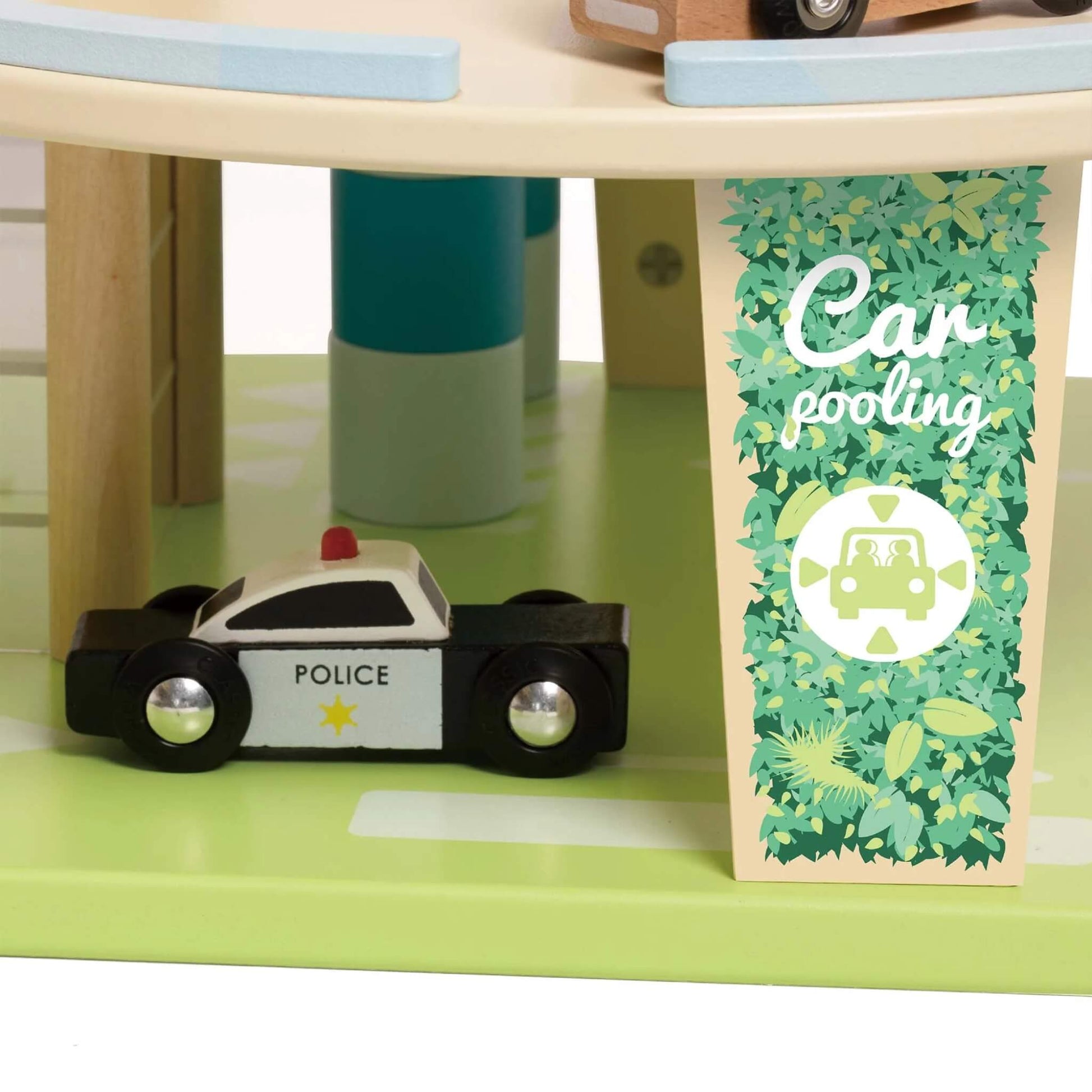 Close-up of a small black-and-white wooden police car parked near a “Car Pooling” sign with green leafy detailing.