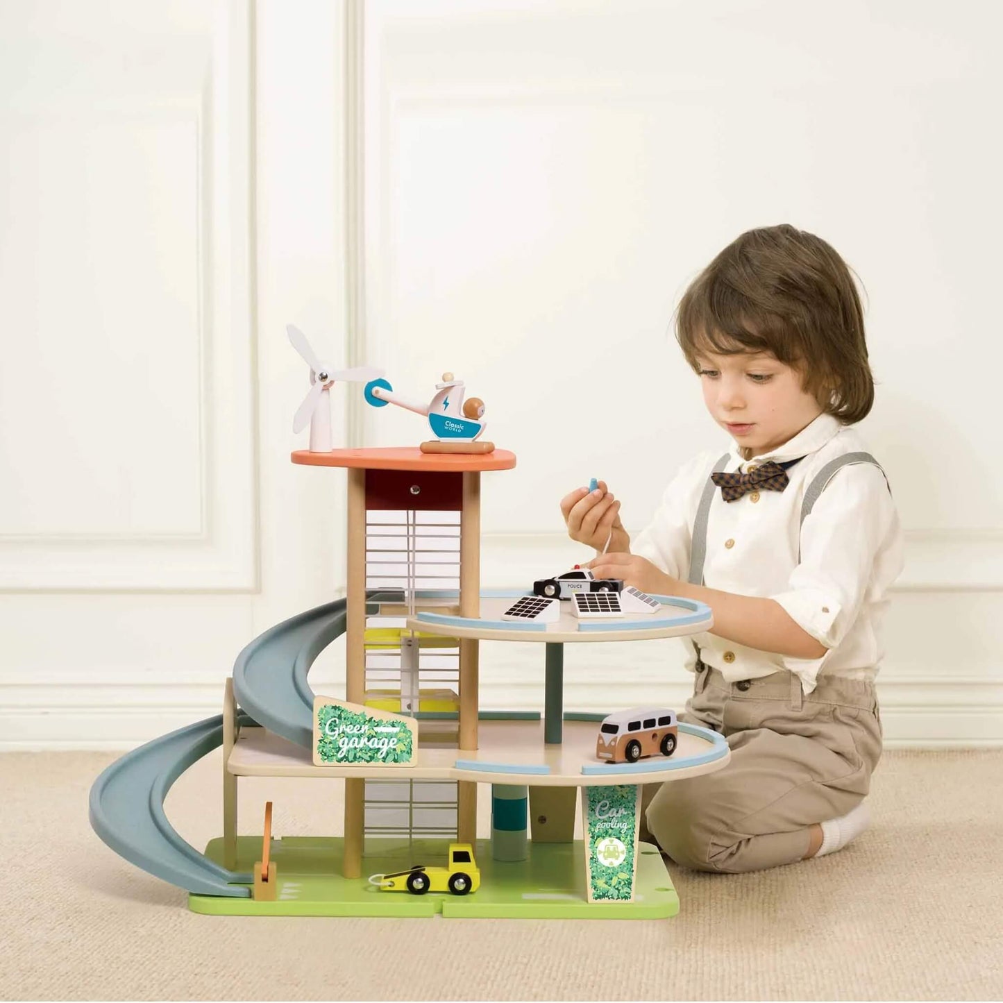 Young child sitting on a carpet, playing with a multi-level wooden garage and toy vehicles, focusing on the top level.