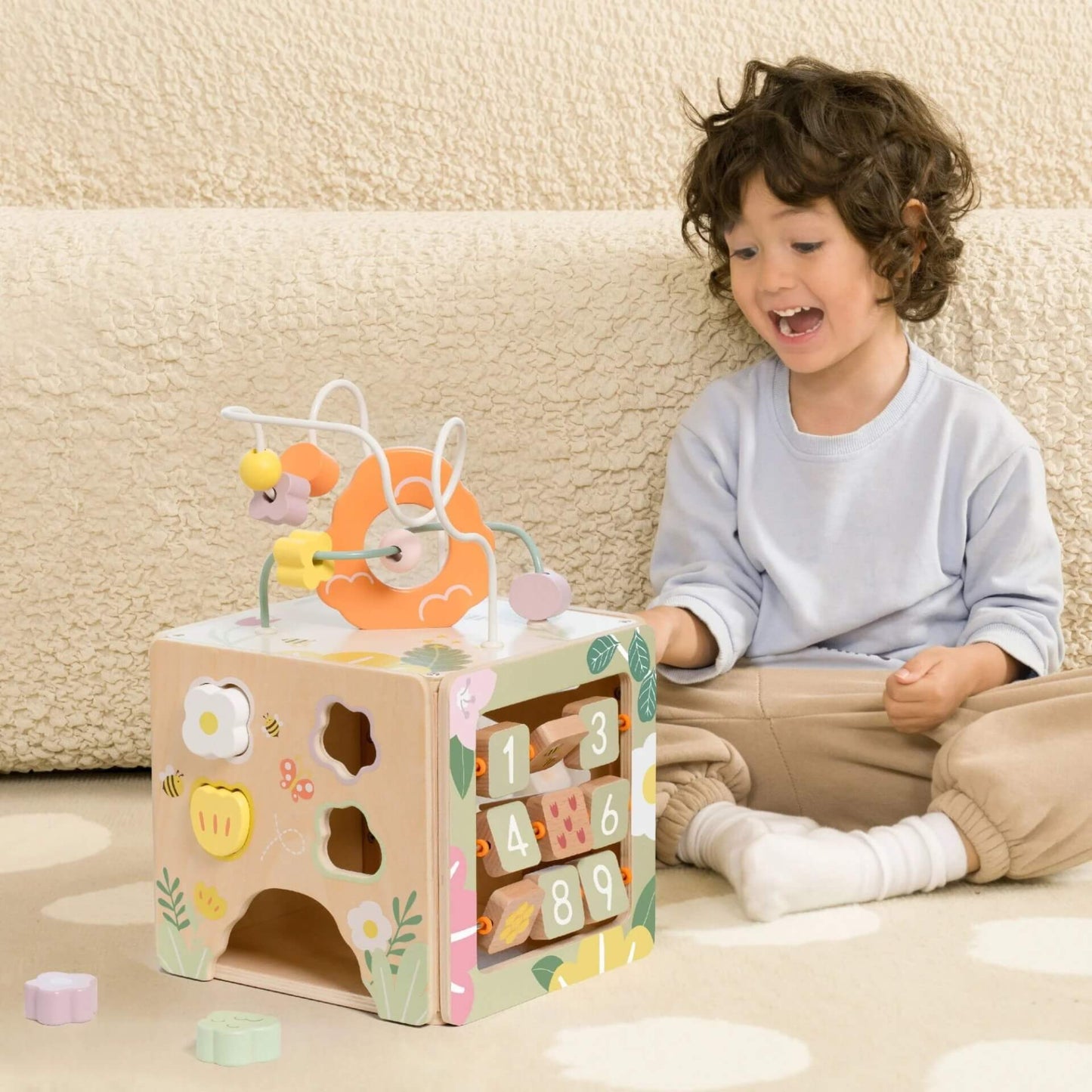 Child playing with a wooden Activity Box, exploring the bead maze, shape sorter, and number flip board.