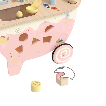 Close-up of the pink cart side panel, featuring shape-sorting cut-outs, a swirl design wheel, and small wooden blocks shaped like sweets on the floor.