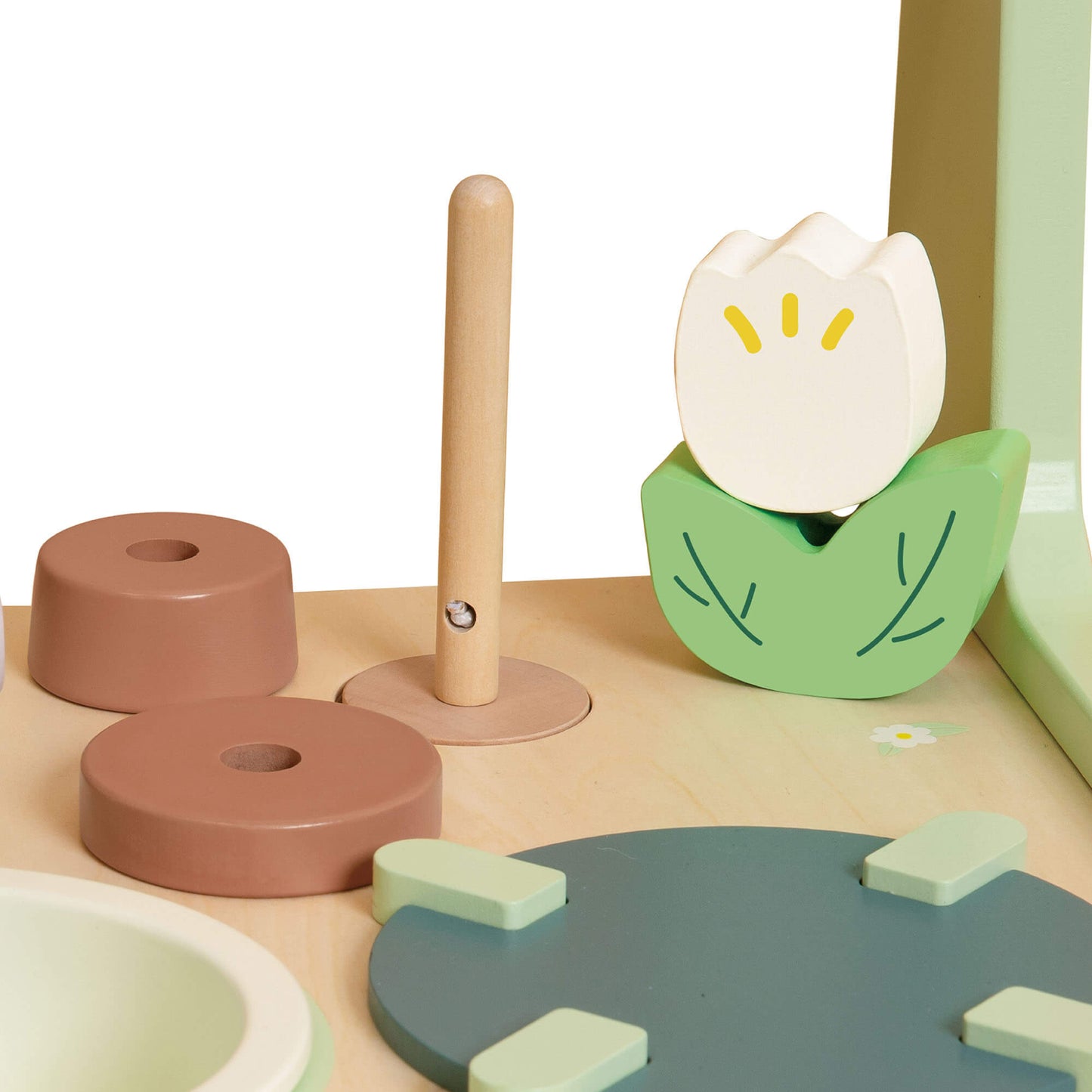 Close-up of a flower-shaped faucet, wooden knobs, and pastel cooking accessories on a toy kitchen worktop.