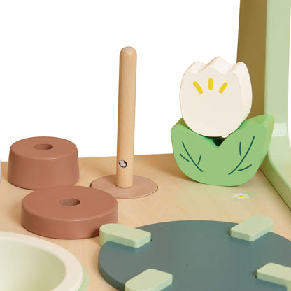 Close-up of a flower-shaped faucet, wooden knobs, and pastel cooking accessories on a toy kitchen worktop.