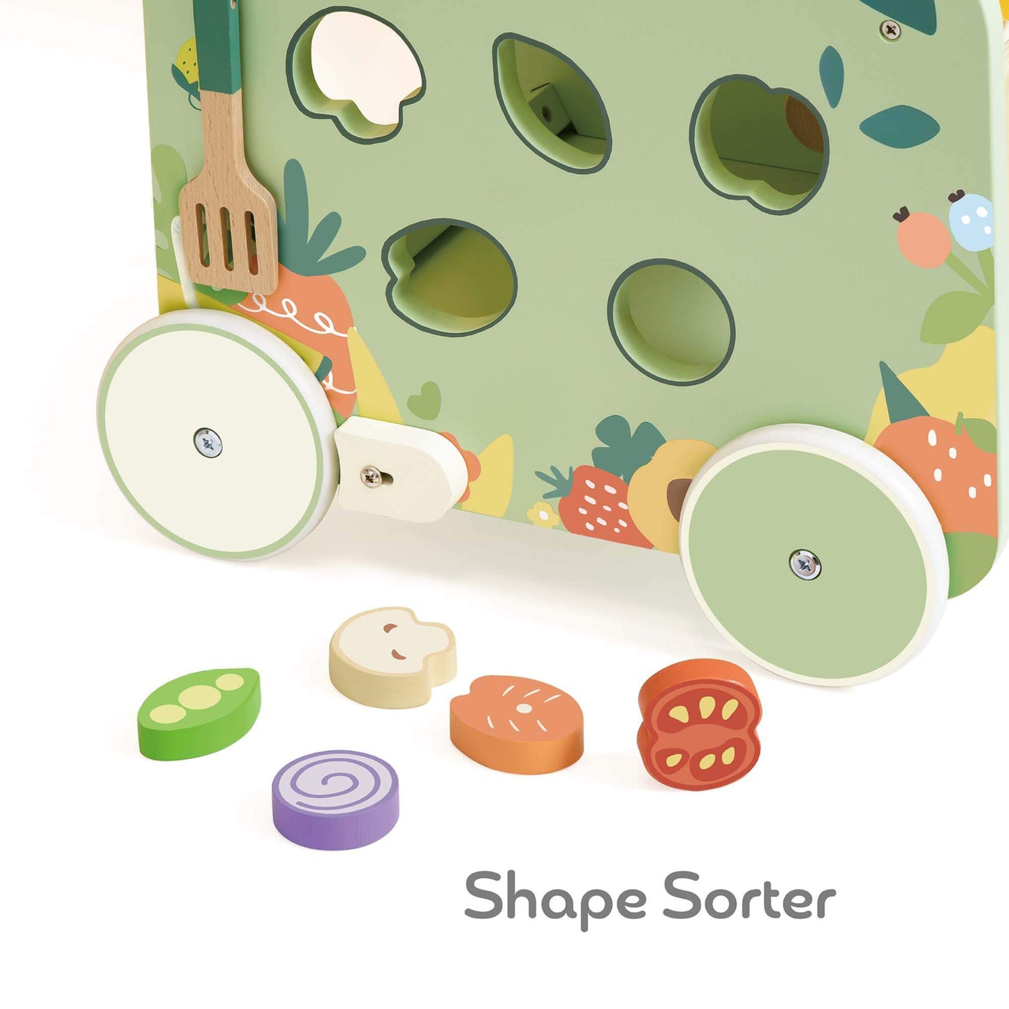 View of a green side panel with vegetable-shaped wooden pieces, including pea pod, onion, and tomato, next to matching cut-out holes.