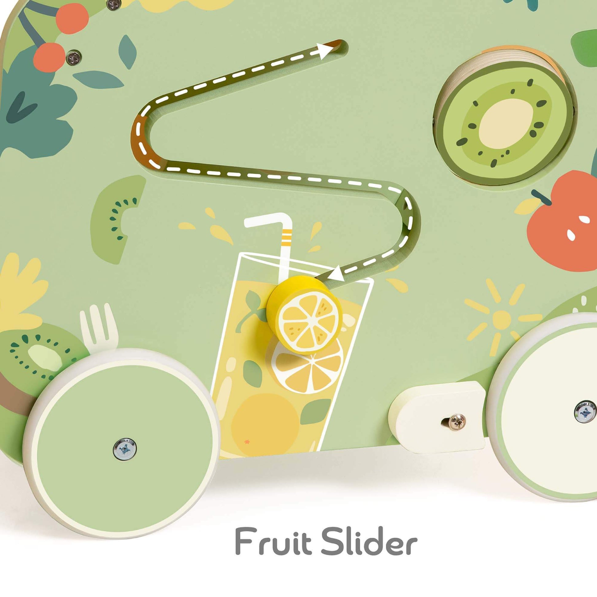 Close-up of a green wooden panel with a winding maze track, showing a yellow wooden lemon slice sliding along a printed fruit drink design, next to a kiwi disc and red apple illustration.