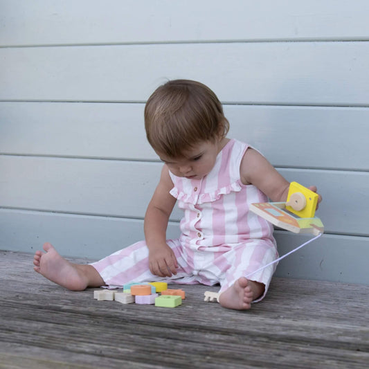 Toddler focused on a wooden house toy, lifting the yellow locking door while pastel geometric blocks are spread out in front.