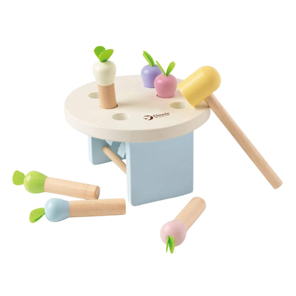 Wooden pounding toy with pastel radish pieces halfway pushed through holes, a yellow mallet resting nearby.