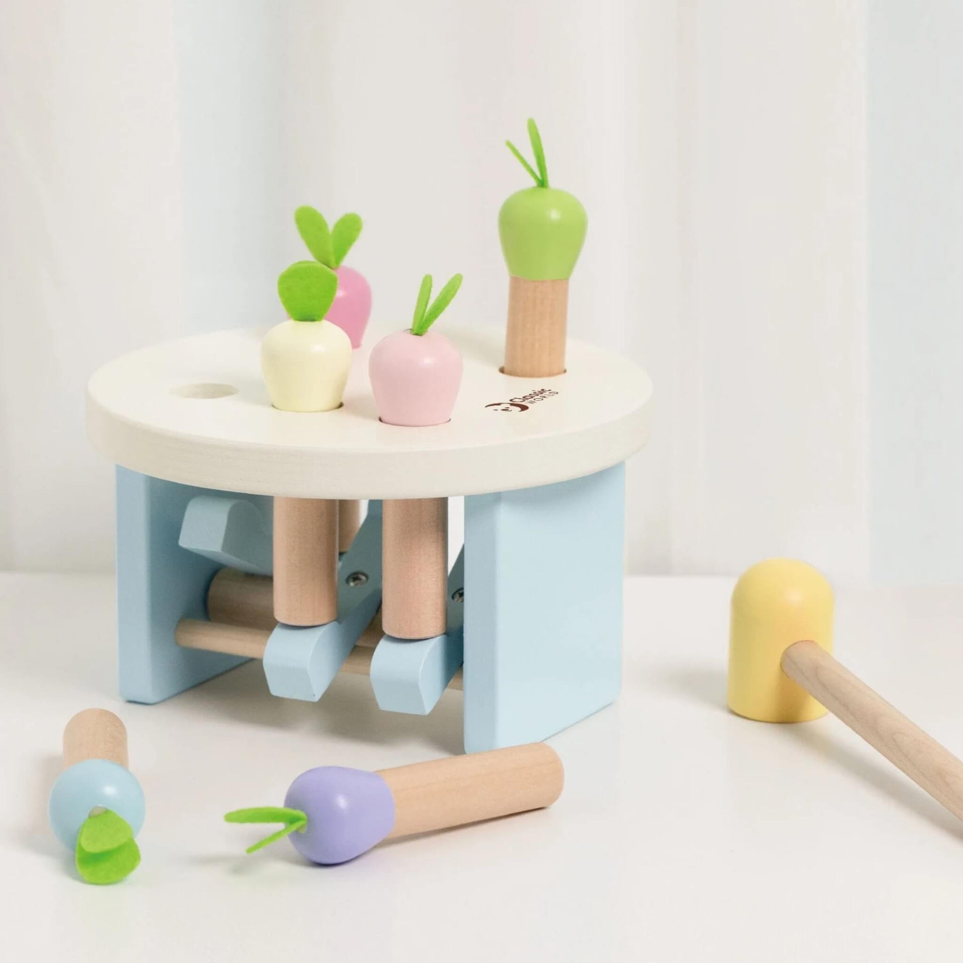 Wooden pounding toy set on a white surface, with radish pieces scattered around and a pastel yellow mallet at the side.