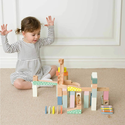 Young child in a striped dress raising hands excitedly while playing with a colourful marble run.