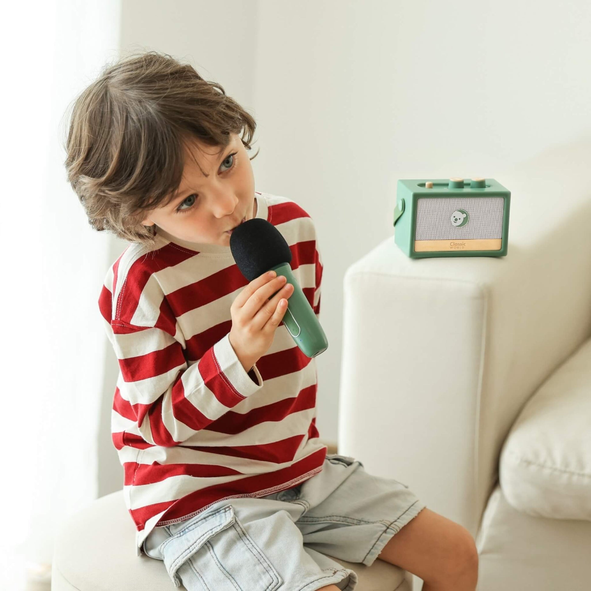 Young child holding microphone and singing while speaker sits nearby, demonstrating imaginative performance play.