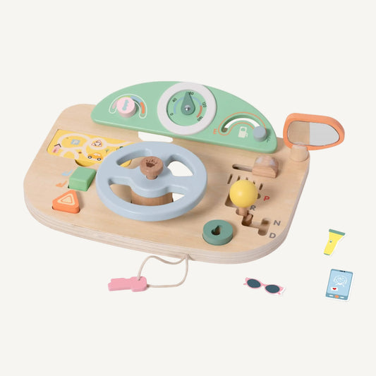 Wooden toy driving dashboard with steering wheel, gear selector and mirror shown at an angle with small play accessories nearby.