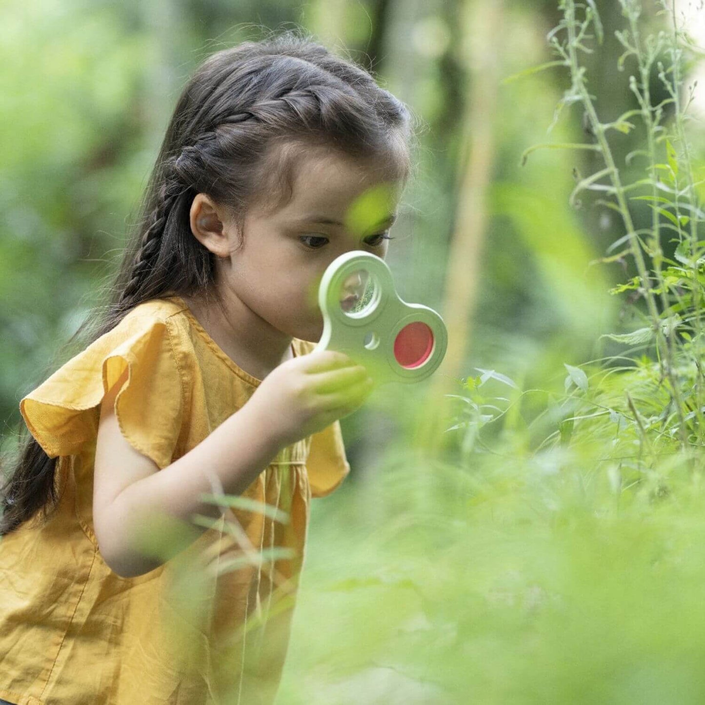 A child exploring nature with the wooden exploration set, using a magnifying tool to examine plants closely outdoors.