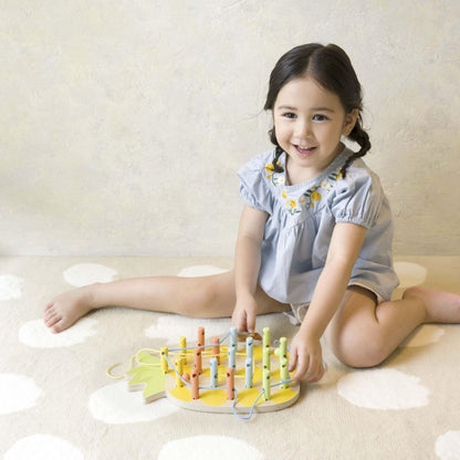 Smiling child playing with a wooden pineapple shaped Linking Game, threading colourful strings through pegs, enjoying creative playtime.