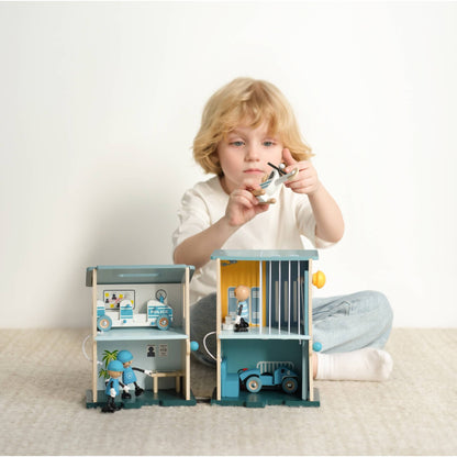 Child playing with wooden police station toy set, holding helicopter above building during imaginative play.