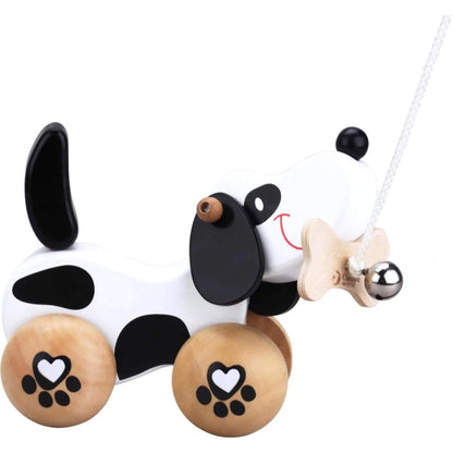 The Classic World Pull-Along Dog is a wooden black and white puppy toy on wheels, with floppy ears, a wagging tail, and a bone in its mouth attached to a pull string.