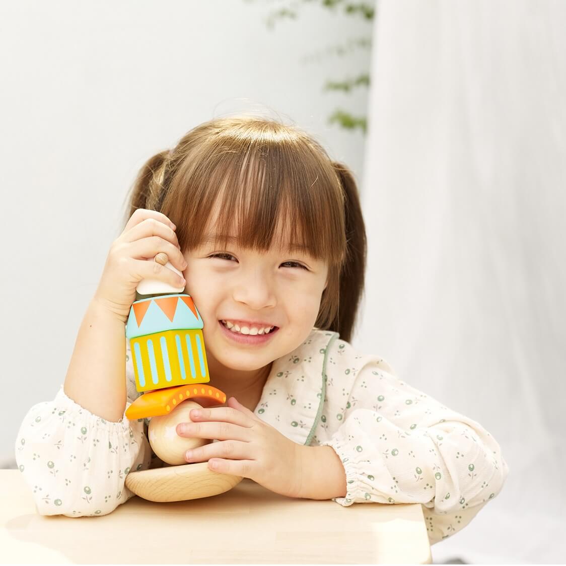 A smiling child holding a completed stacking and balancing clown toy, showcasing its colourful wooden design and playful features.