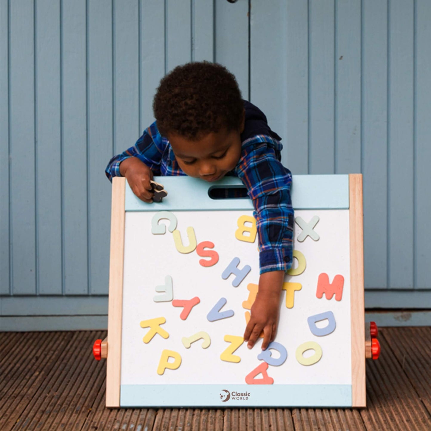 Young child placing colourful magnetic letters onto whiteboard easel, encouraging fine motor skills and letter recognition.