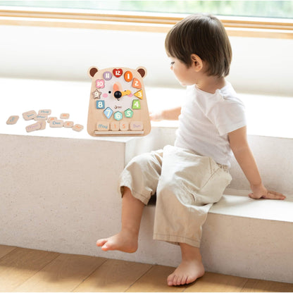 Young child sitting beside wooden clock learning toy with removable number pieces and date tiles encouraging early time learning.