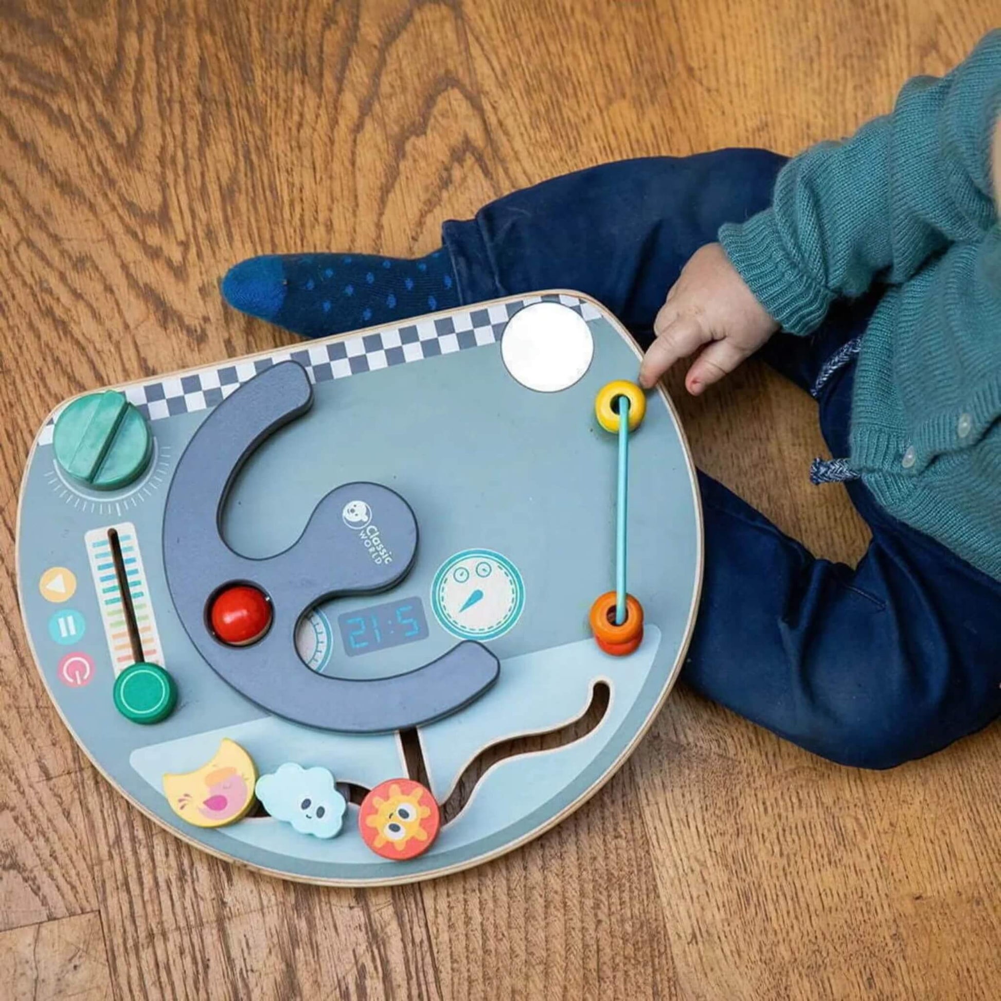 Overhead view of a toddler playing with a busy board on wooden flooring, touching the sliding beads.
