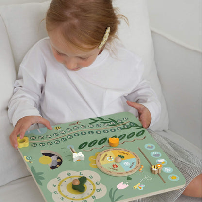 Young child sitting on a sofa playing with a pastel green wooden learning board, moving the dials and sliders to explore days, months, and weather.