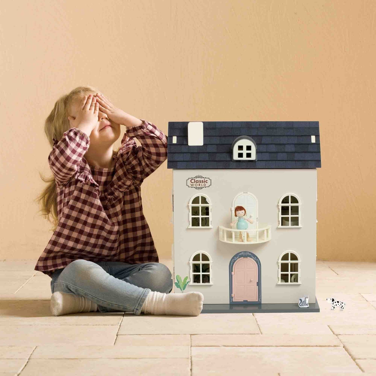 Child sitting next to the Classic World Vintage Doll House, featuring a charming exterior with a balcony, detailed windows, and playful accessories.