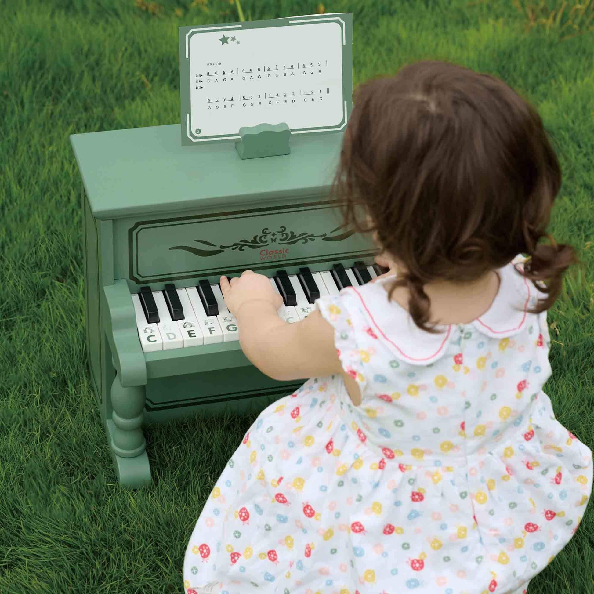 A child playing a vintage design wooden piano in green. Includes a sheet music holder. Encouraging early musical learning.