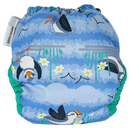 A newborn reusable nappy shown from the back with gathered elastic and a blue puffin-themed print featuring birds, clouds and flowers.