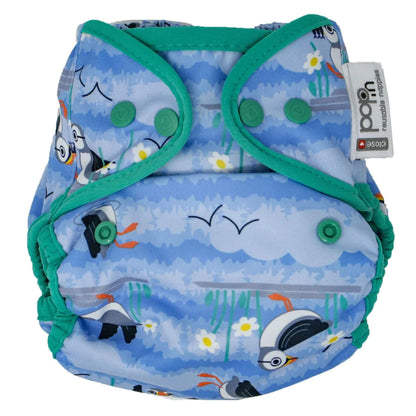 Close pop-in reusable nappy cover featuring a light blue background with puffin illustrations, green edging, and green popper fastenings on the front panel.