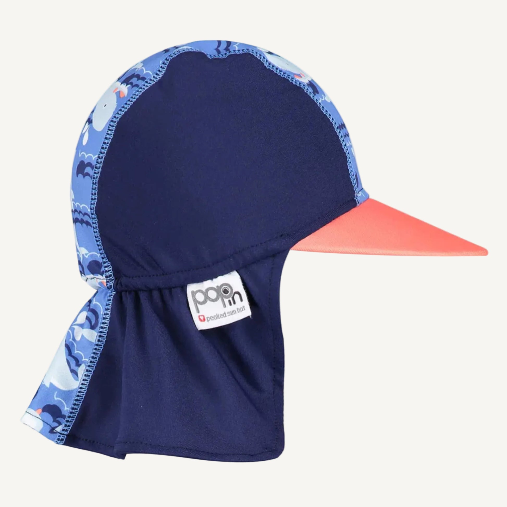 A navy sun hat shown from the side with a coral peak, a whale-patterned top section and a long legionnaire-style back panel.