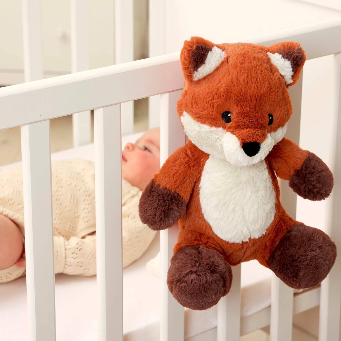Baby lying in a white cot while a plush fox sound soother is attached securely to the cot rail, positioned within the baby’s view.