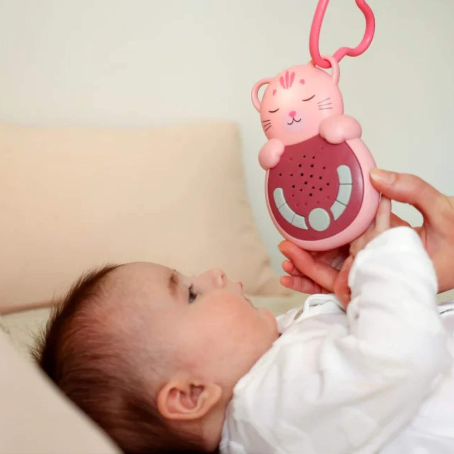 A baby lying comfortably while holding a pink cat-shaped baby sleep aid, demonstrating its portable size and easy grip during rest.