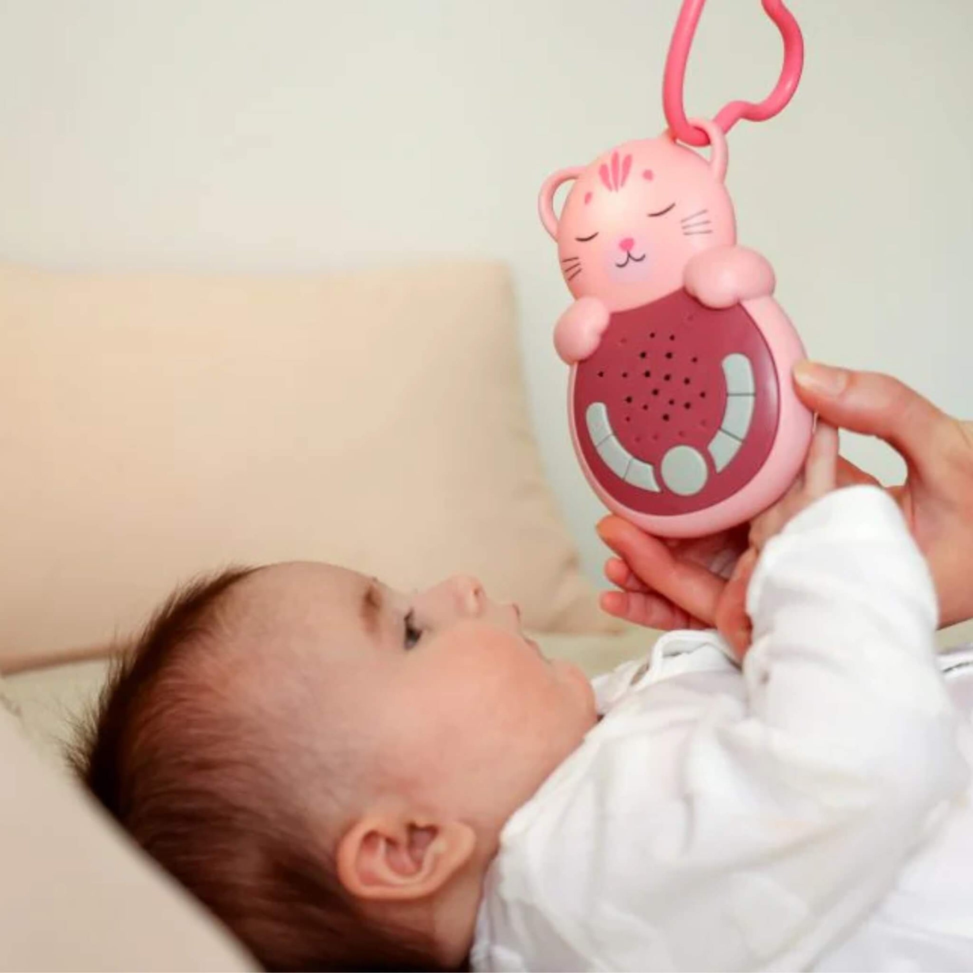 A baby lying comfortably while holding a pink cat-shaped baby sleep aid, demonstrating its portable size and easy grip during rest.