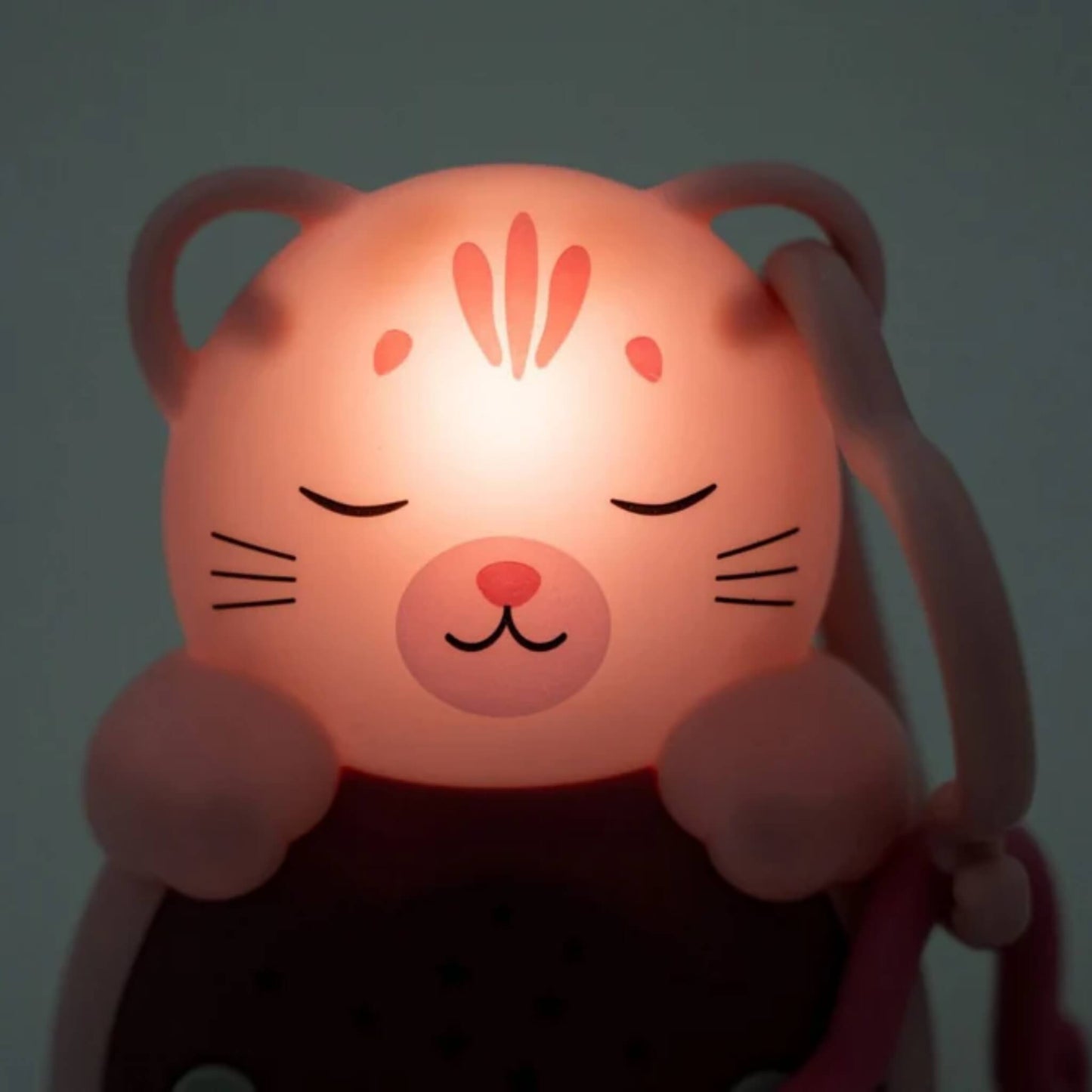 Close-up of a softly glowing cat night-light with eyes closed, radiating a warm red light from its face in a darkened setting.