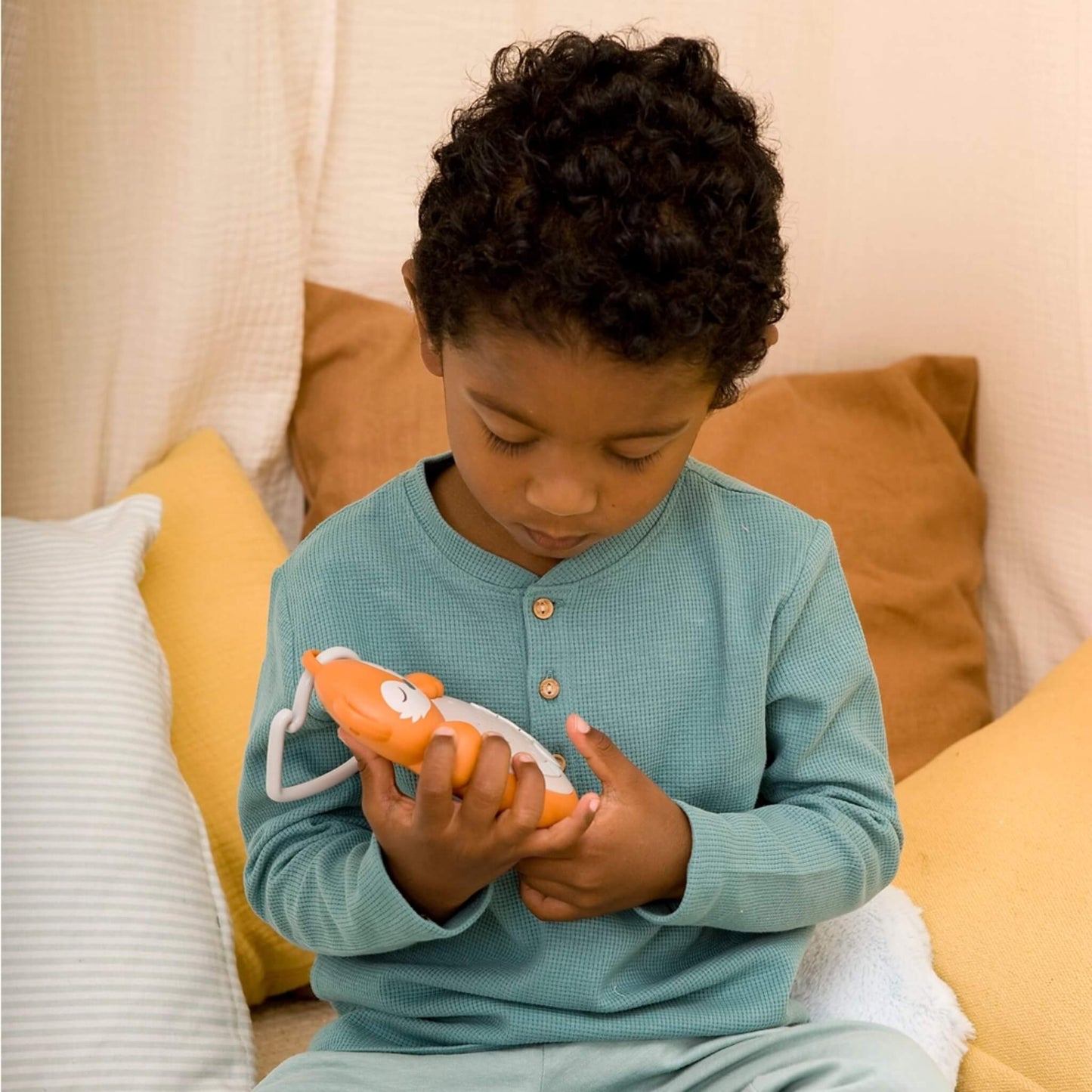 A child sitting on a bed in soft loungewear, looking closely at the fox-shaped sleep aid held in both hands, demonstrating its use in a cosy setting.
