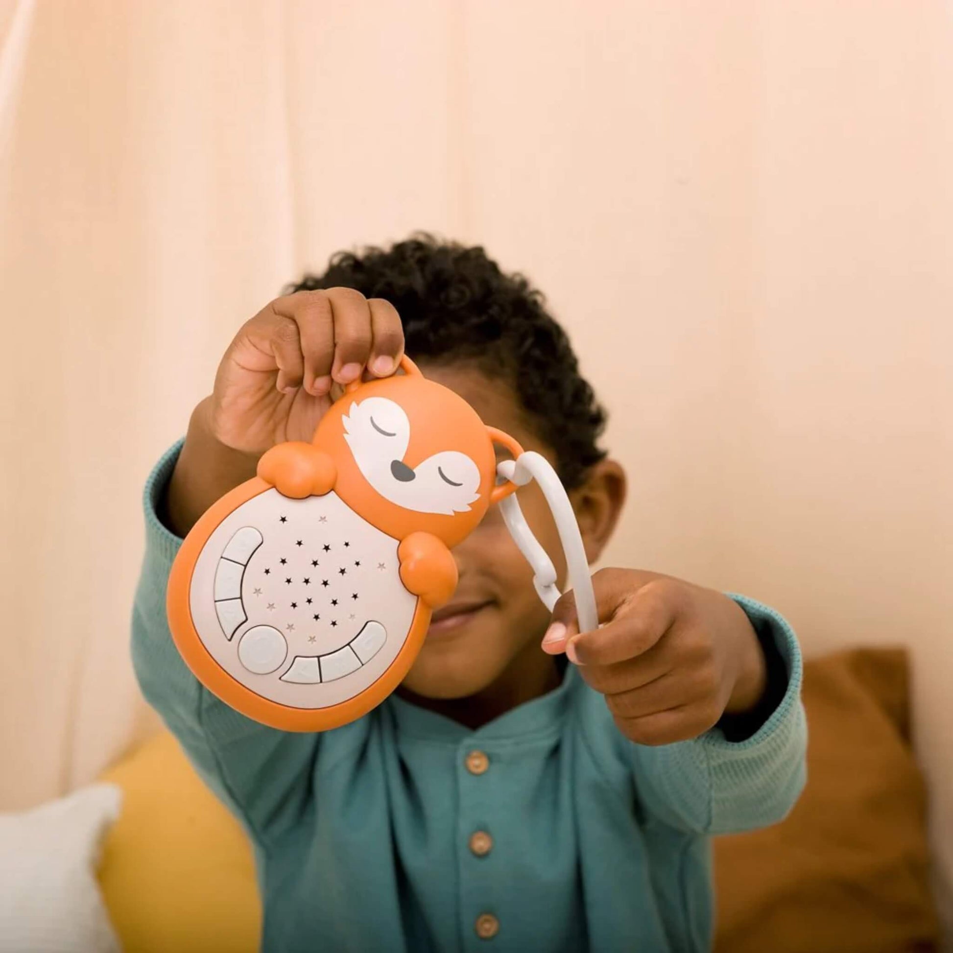 A young child holding up the fox-shaped sleep aid by its clip, smiling and showing its lightweight, easy-to-carry design.