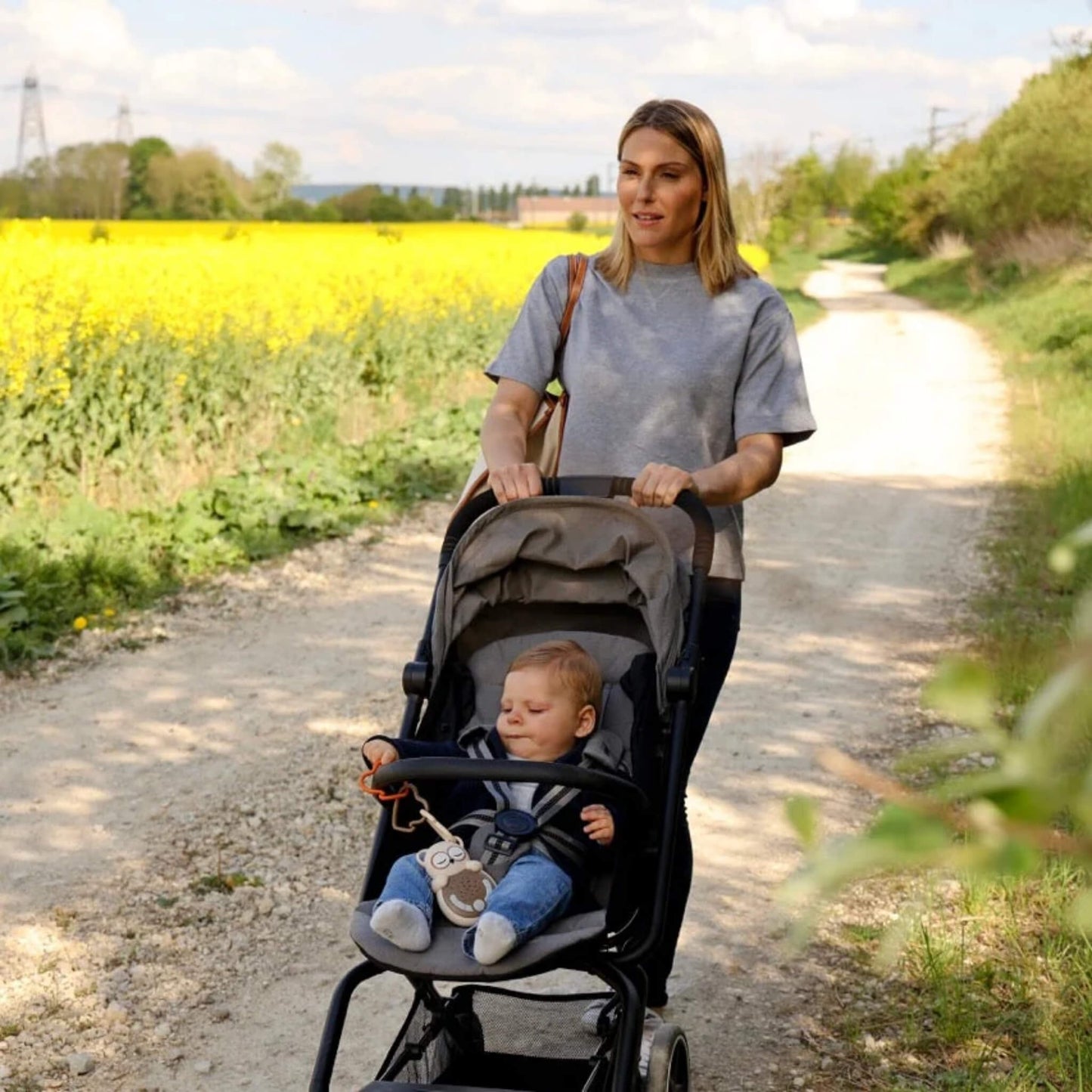 Woman pushing a stroller with a baby in a field of yellow flowers.