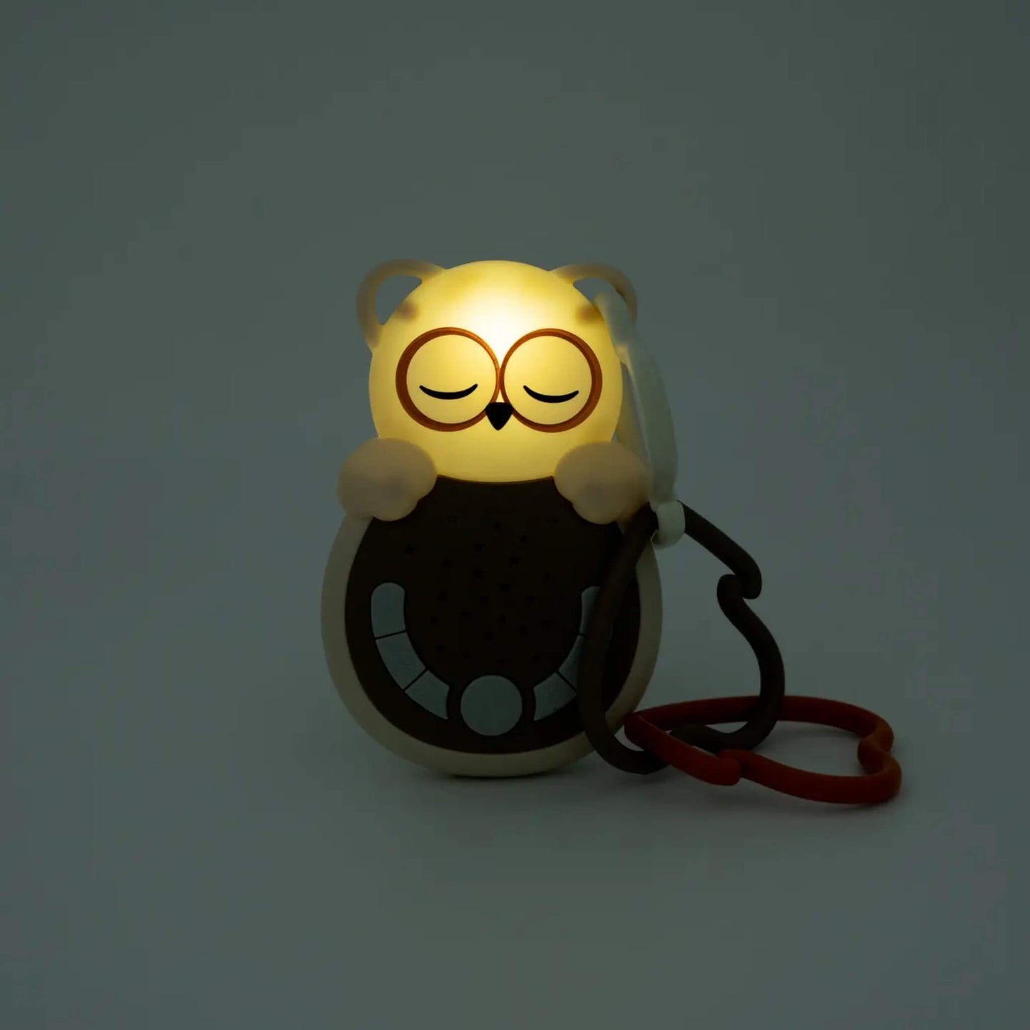 A portable owl-shaped baby sound machine glowing with a soft amber night light set against a darkened background.