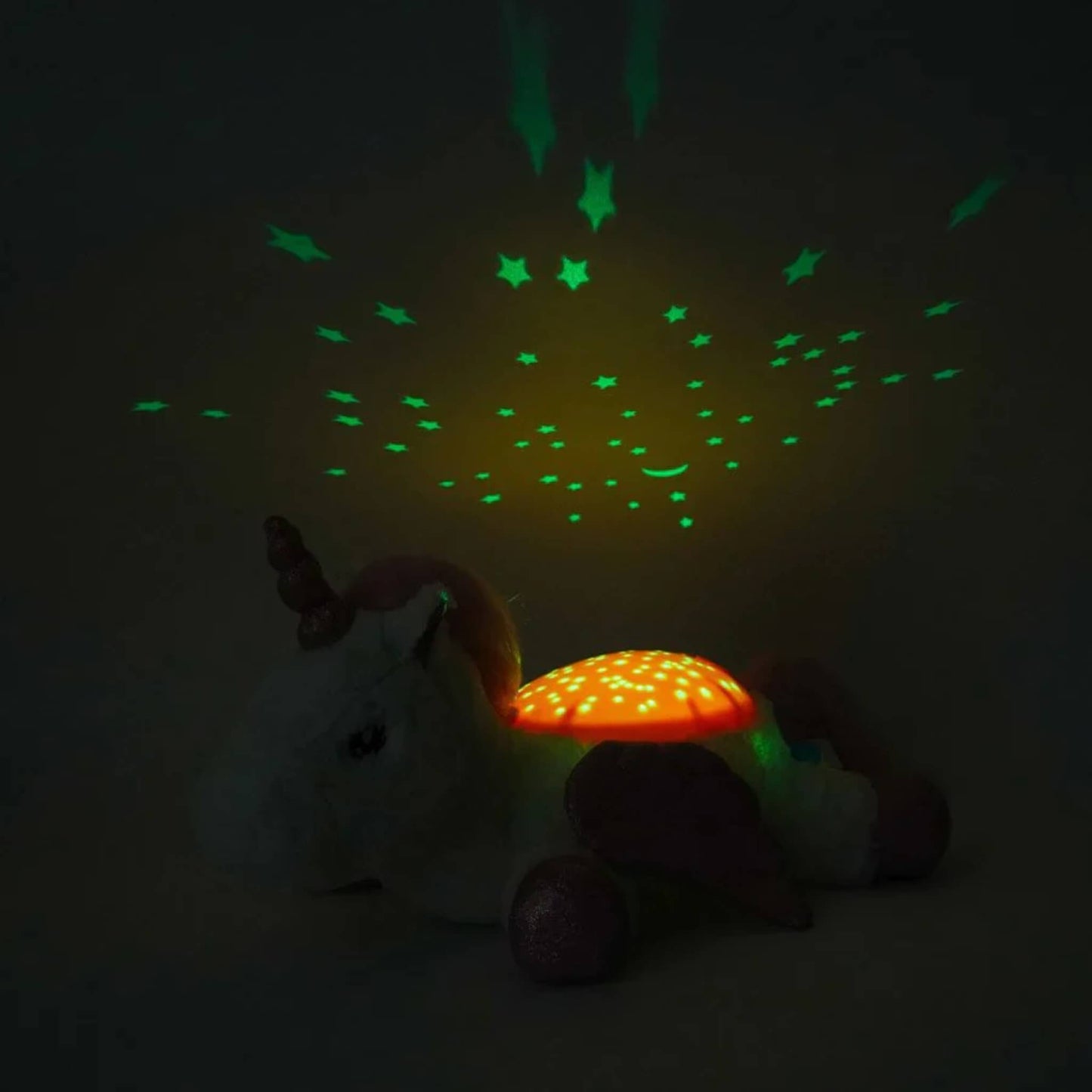A unicorn night light in a dark room projecting green stars and a crescent moon onto the ceiling while the pink dome glows amber.