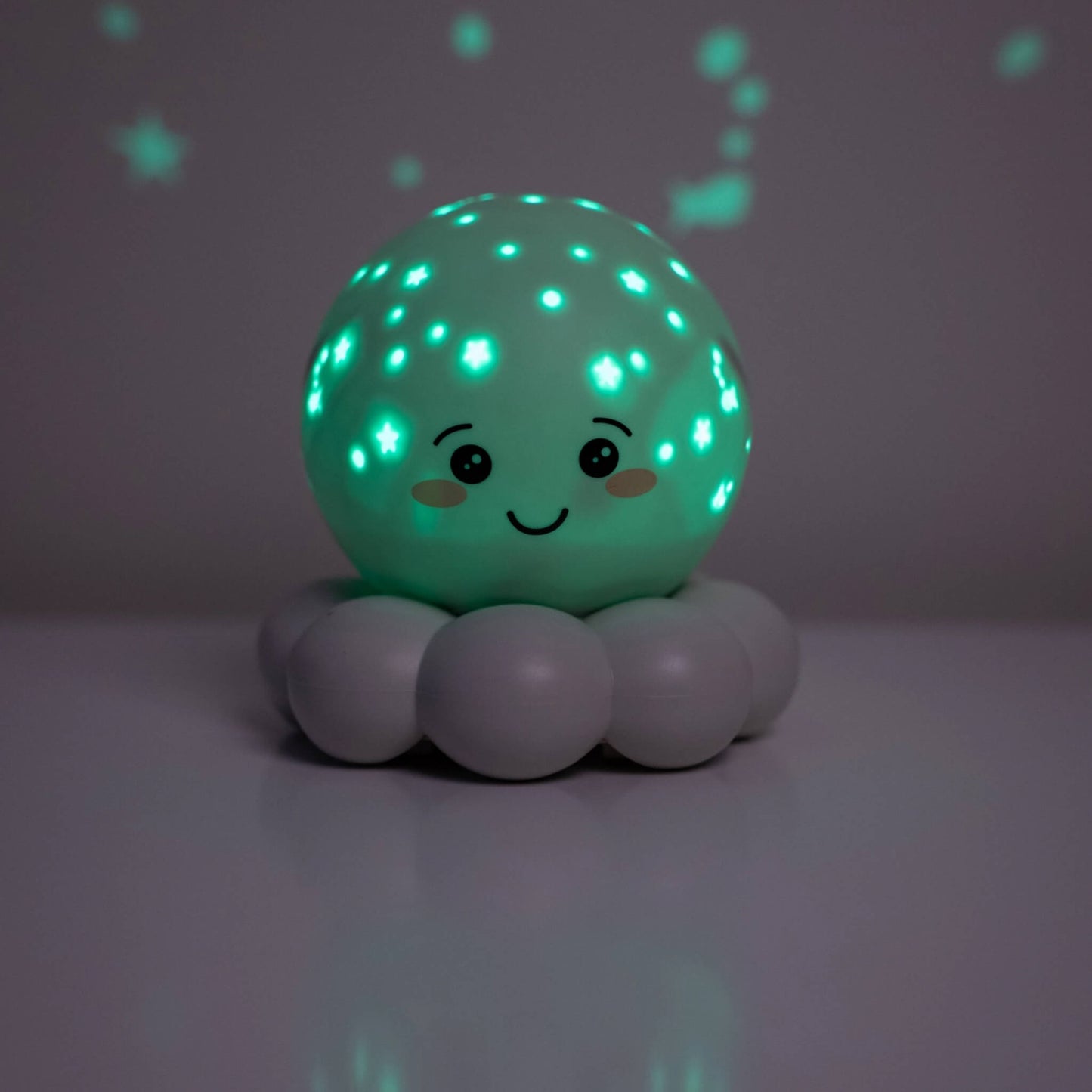 A cute, smiling spherical night light with a mint green glowing face and star patterns, resting on a grey cloud-shaped base against a dark grey background.