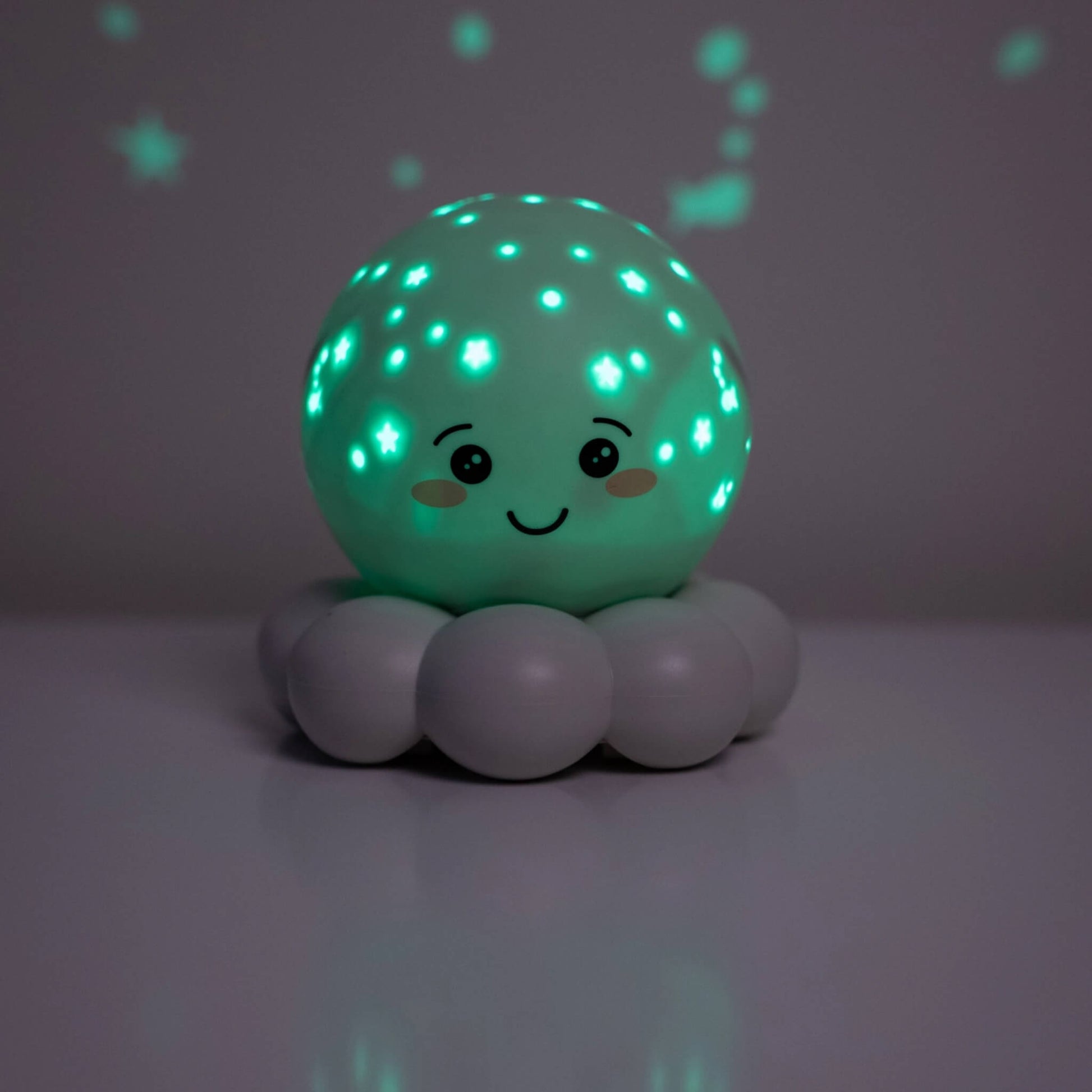 A cute, smiling spherical night light with a mint green glowing face and star patterns, resting on a grey cloud-shaped base against a dark grey background.